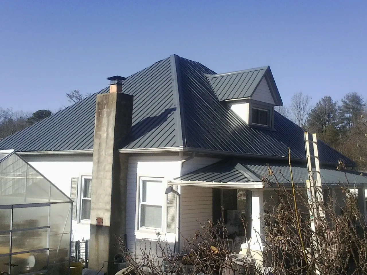 Dark blue standing seam metal roof on a white farmhouse with dormer — Slate & Tile Roof Repair by Roofing Brothers in Prairie Grove