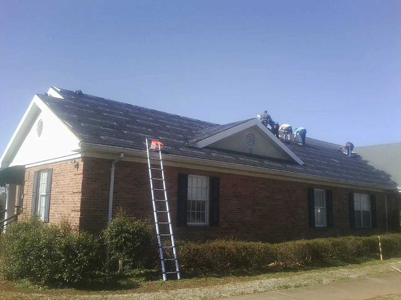 Crew tearing shingles off a brick ranch roof with a ladder set — Metal Roof Repair work by our crew in Prairie Grove