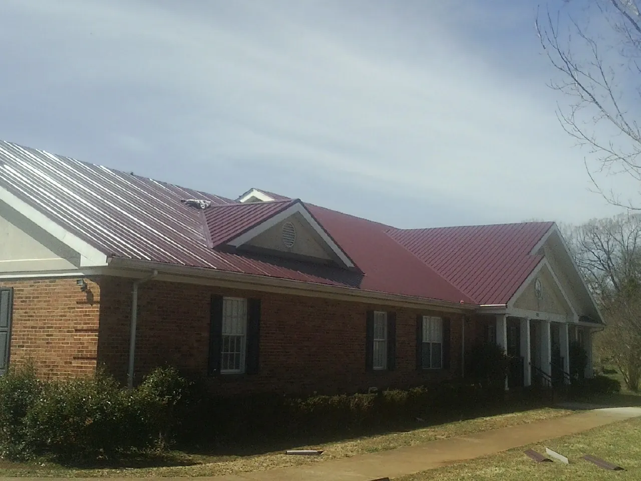 Red metal roof with gabled entries on a long brick building, from a Hail Damage Roof Repair job in Prairie Grove