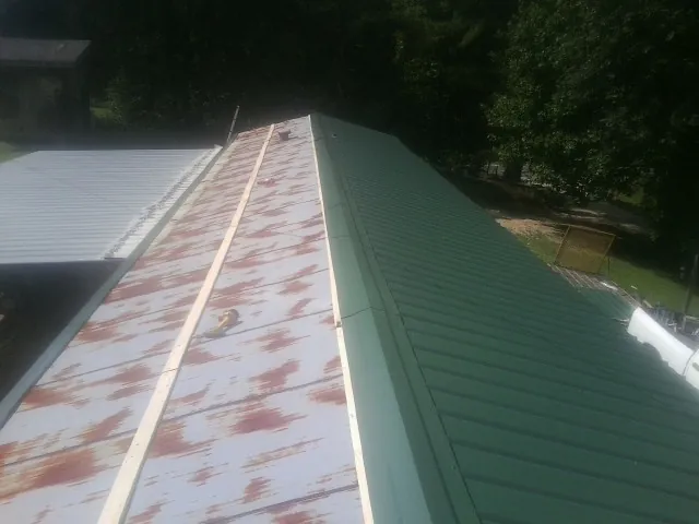 Old rusted panels beside newly installed green metal roofing — Wind Damage Roof Repair by Roofing Brothers in Prairie Grove