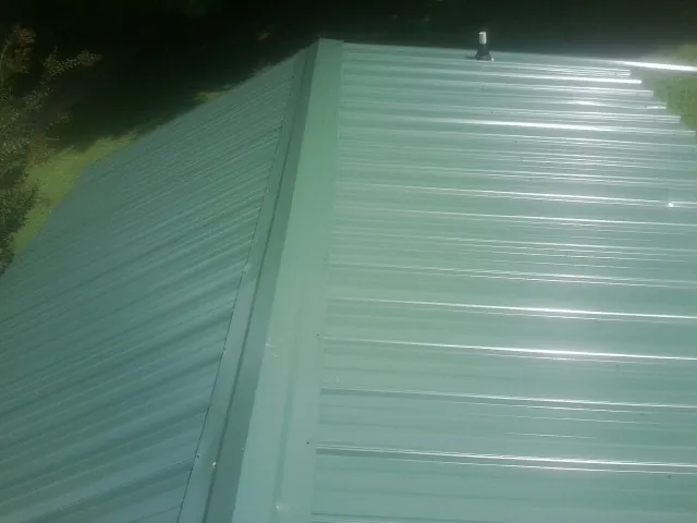 New green metal panels meeting at the ridge of a roof — Flat Roof Repair work by our crew in Prairie Grove