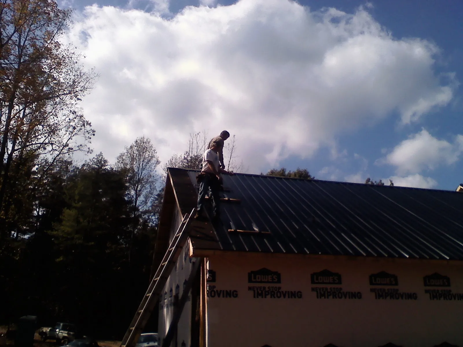 Roofer fastening dark metal panels high against a cloudy sky, from a Roof Inspection job in Prairie Grove