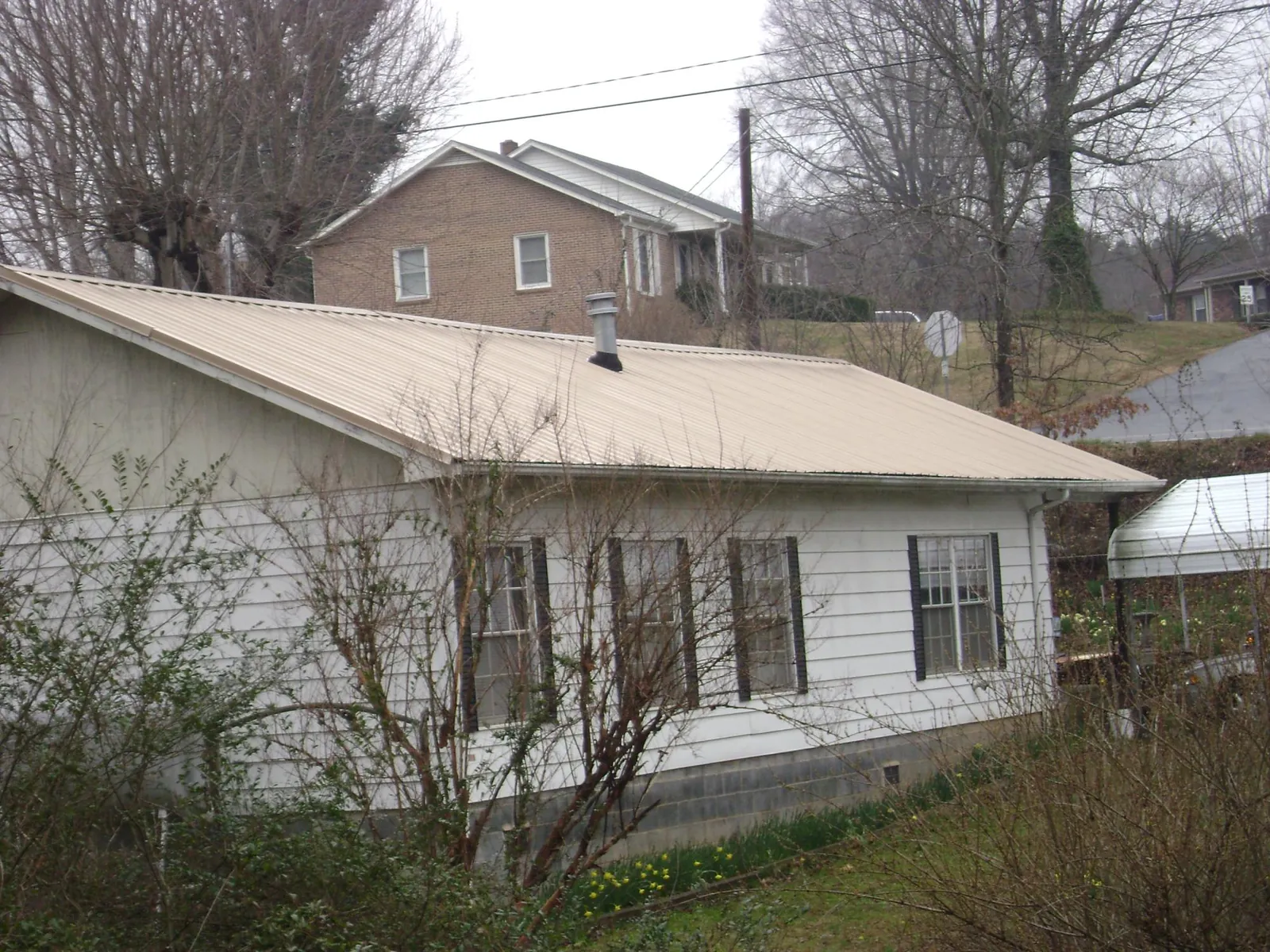 Tan metal roof on a white sided house set into a hillside — Commercial Roofing by Roofing Brothers in Prairie Grove