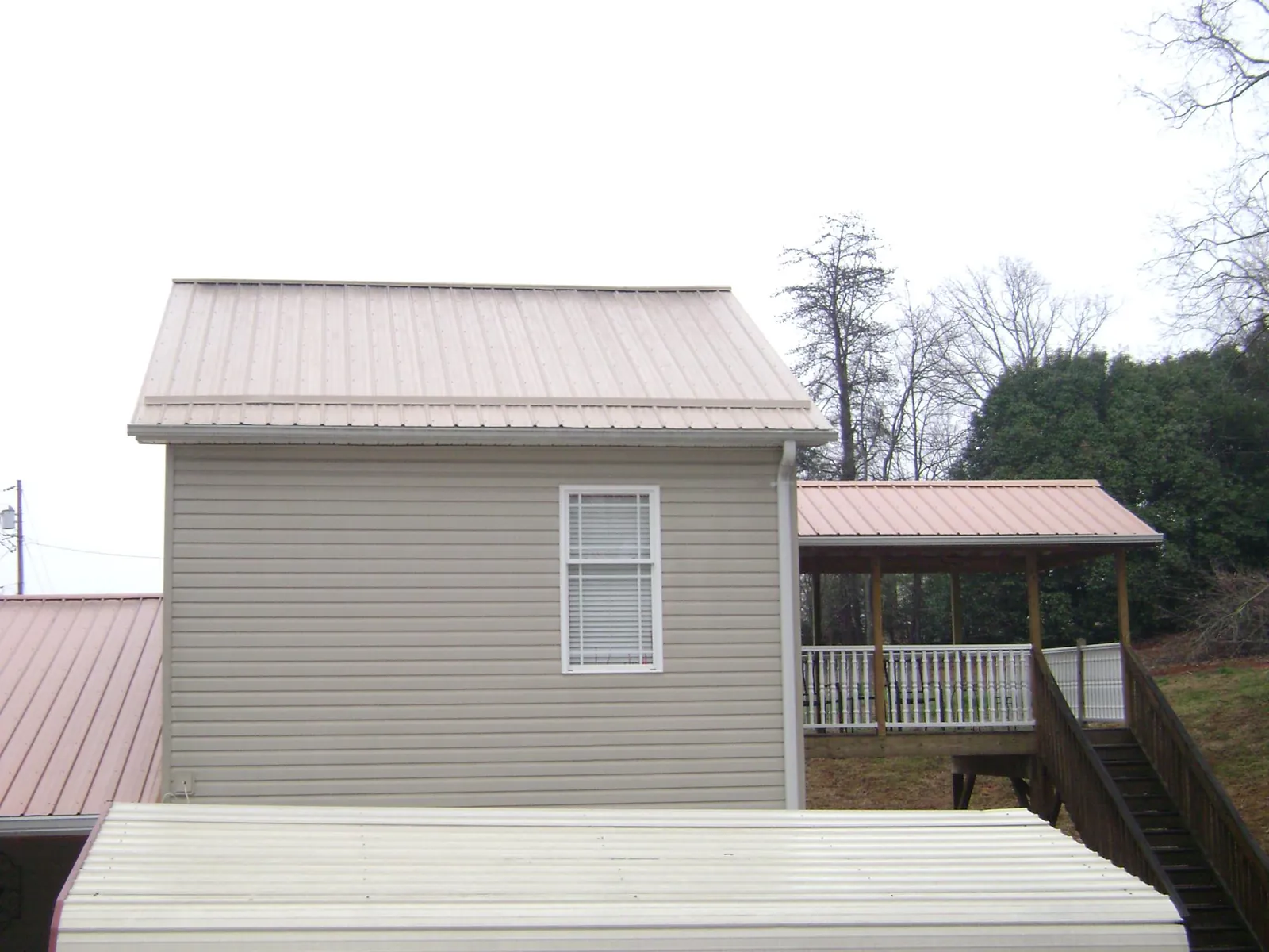 Tan metal roofs on a two story addition and attached porch, from a Roof Replacement job in Prairie Grove